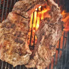 Två saftiga bitar grillad iberico-karré fräser över glödande kol. Flammorna slickar köttet och ger det en perfekt yta.