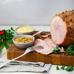 En saftig julskinka, redo att grilla, med senap och julpynt.