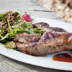 Grillad vildsvin ryggbiff med en fräsch sallad på quinoa och gröna blad, serverad med en smakrik sås.