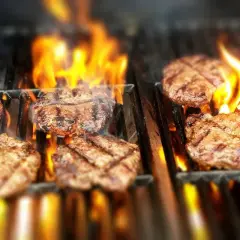 Flera saftiga hamburgare grillas på en gasolgrill med flammande eld.