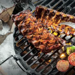 Grillade revbensspjäll med grönsaker över glödande kol. En gaffel sticker upp ur köttet. Snö och ved i bakgrunden. Perfekt för ett salt lag.
