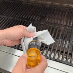 Händer oljar in grillgallret med en pappersduk och en flaska rapsolja för att maten inte ska fastna.