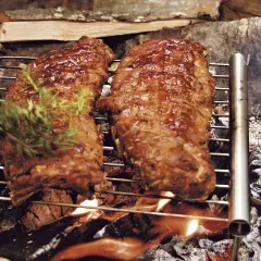 Två saftiga grillade spareribs på ett grillgaller över öppen eld. En kvist rosmarin läggs på för extra smak.