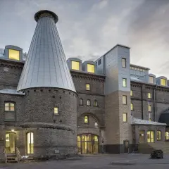 Imponerande tegelbyggnad med ett konformat torn, likt en gigantisk tuva av **panicum virgatum** mot en dramatisk himmel.
