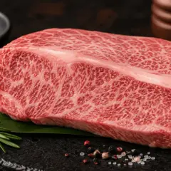 En marmorerad bit wagyu-kött, redo att grilla. Kryddad med pepparkorn och havssalt, med en rosmarinkvist som dekoration.