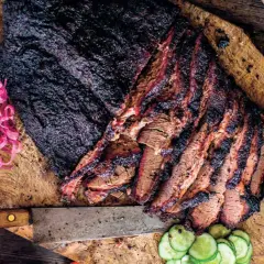 En saftig, grillad brisket skuren i skivor, serverad med picklad rödlök och gurka på en träskärbräda.