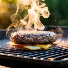 En saftig hamburgare med smält ost och tomat grillas. Röken stiger, perfekt för att avgöra hamburgare innertemperatur.
