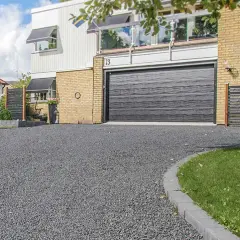 En grå stenlagd uppfart leder fram till ett modernt hus med garageport. Perfekt uppfart inspiration för en stilren entré.