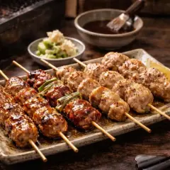 Läckra yakitori kycklingspett med en glansig sås och sesamfrön, serverade på en tallrik med citronklyfta.