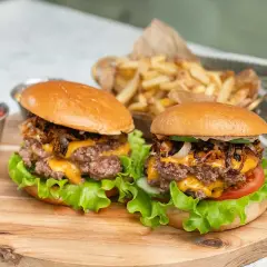Två saftiga hamburgare med ost och krispiga lökar, redo att grillas. Serveras med pommes frites och ketchup.