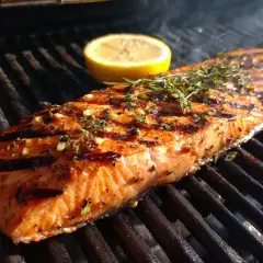 En saftig bit saltlag lax grillas med citron och örter. Röken stiger från grillen.