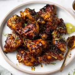 En tallrik med glaserade kycklingvingar, toppade med lime och örter. En sked med glaze ligger bredvid.
