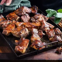 En bricka med saftiga revbensspjäll, täckta av en glansig revbens glaze. Kryddor som kanel och stjärnanis ligger bredvid.