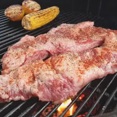 Två bitar grillad secreto med majskolv och citronklyftor på grillen.