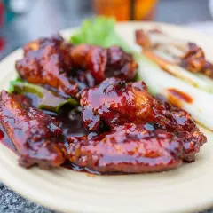 Saftiga kycklingvingar täckta med en glansig, mörk egen barbequesås, serverade med selleristavar och sallad.