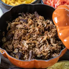 Saftigt pulled pork i en orange gryta, redo för grillen. Serveras med tillbehör som majs, gurka och tomater.