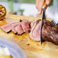 Perfekt grillad ryggbiff skärs upp på en träskärbräda. En grillad citron ligger bredvid.