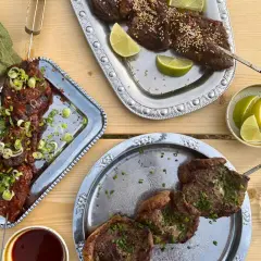 Grillad oxbringa på spett, toppad med salladslök och chiliflakes. Serveras med limeklyftor och sesamfrön.