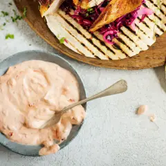 En skål med krämig, rosa hot chilisås bredvid grillade kycklingtacos med rödkål. Perfekt för att addera extra smak!