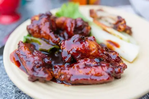 Saftiga kycklingvingar täckta med en glansig, mörk egen barbequesås, serverade med selleristavar och sallad.