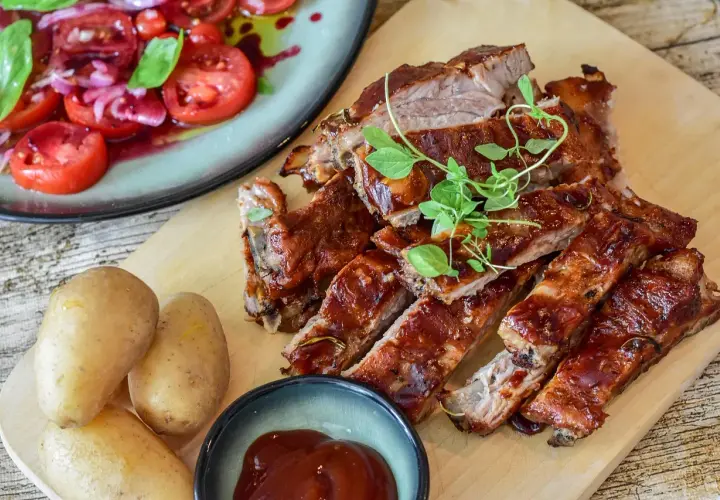 Saftiga revben, perfekt grillade och glaserade, serveras med färsk potatis och en tomat- och löksallad. En härlig måltid att grilla revben till!