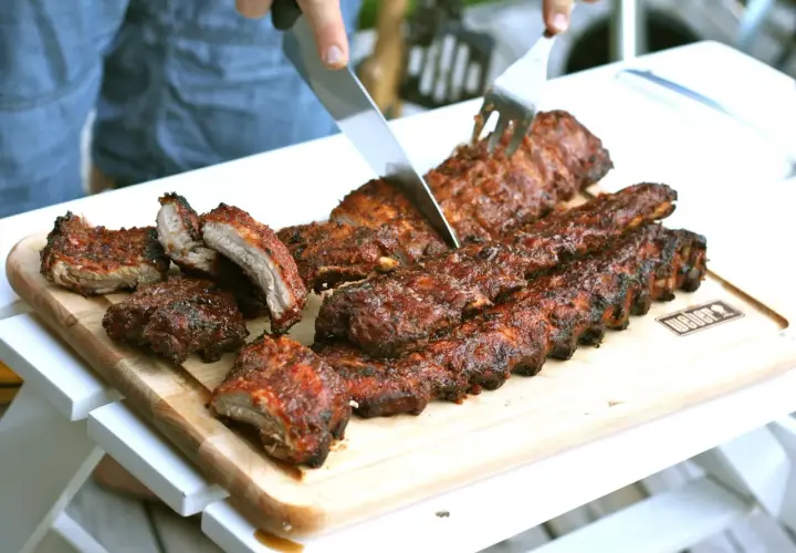 En person skär upp saftiga, grillade kamben på en skärbräda. Perfekt för en sommarkväll med grillning.