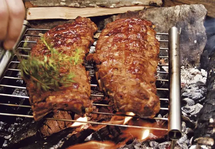 Två saftiga grillade spareribs på ett grillgaller över öppen eld. En kvist rosmarin läggs på för extra smak.
