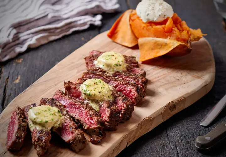 Skivad entrecote rare med smält örtsmör, serverad med sötpotatis och en klick gräddfil.