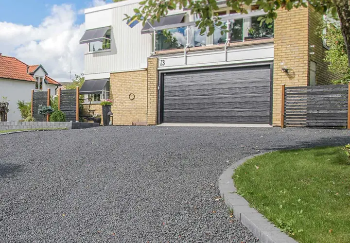 En grå stenlagd uppfart leder fram till ett modernt hus med garageport. Perfekt uppfart inspiration för en stilren entré.