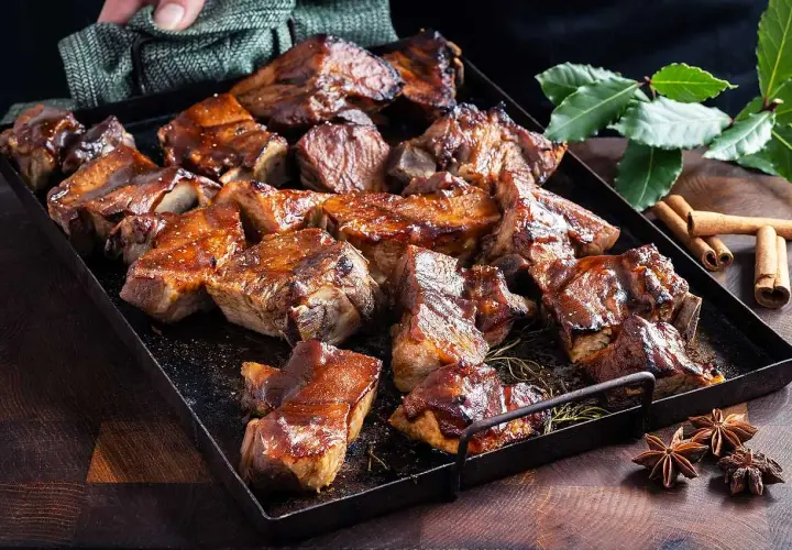 En bricka med saftiga revbensspjäll, täckta av en glansig revbens glaze. Kryddor som kanel och stjärnanis ligger bredvid.