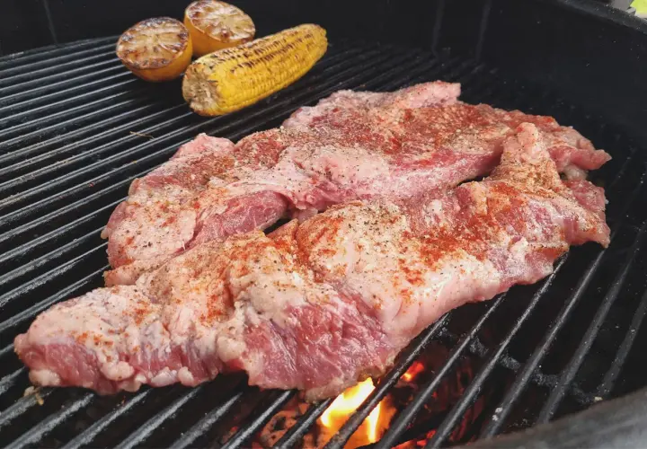 Två bitar grillad secreto med majskolv och citronklyftor på grillen.
