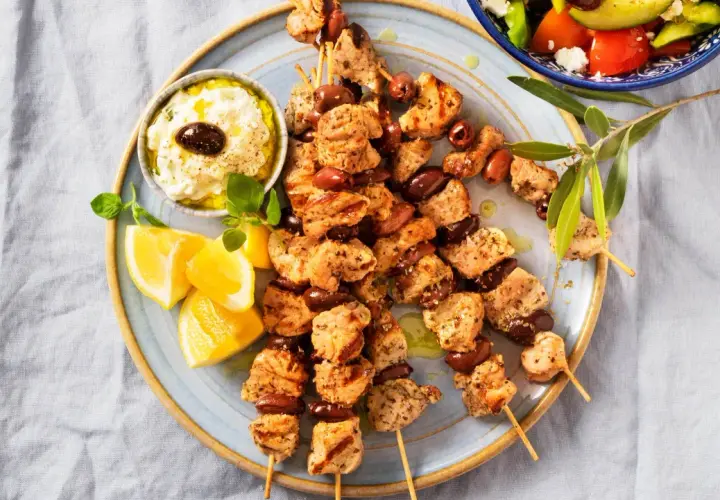 Grillade kycklingspett med oliver, citronklyftor och en krämig dipp. Perfekt för en somrig middag med smak av souvlaki marinad.