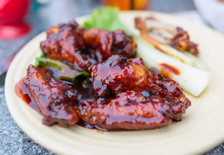 Saftiga kycklingvingar täckta med en glansig, mörk egen barbequesås, serverade med selleristavar och sallad.