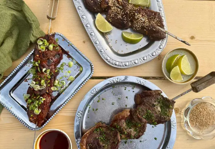 Grillad oxbringa på spett, toppad med salladslök och chiliflakes. Serveras med limeklyftor och sesamfrön.