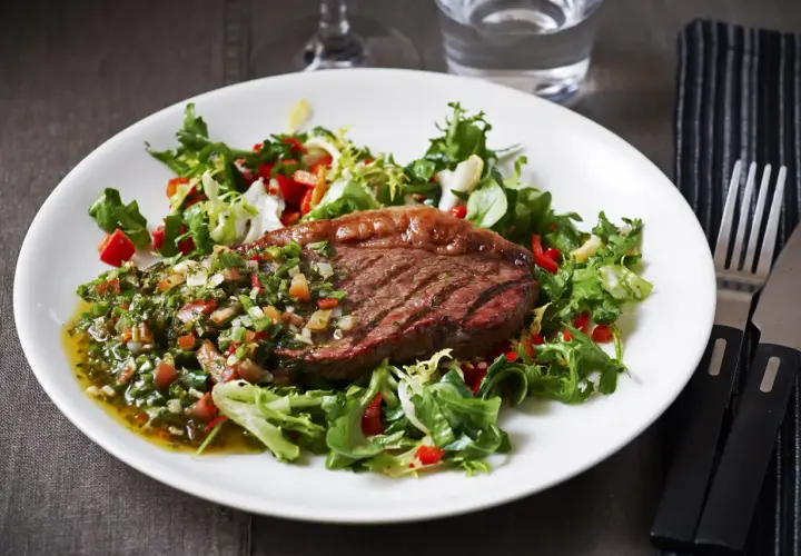 Grillad picanha styckdetalj serverad med en fräsch sallad och chimichurrisås.
