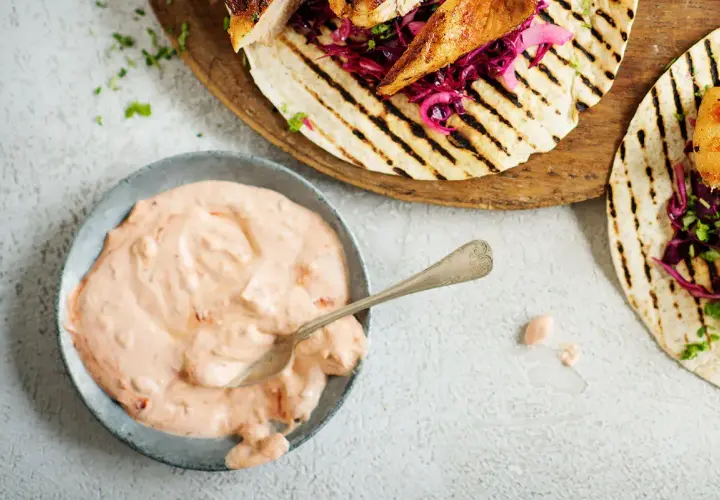 En skål med krämig, rosa hot chilisås bredvid grillade kycklingtacos med rödkål. Perfekt för att addera extra smak!