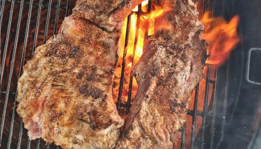 Två saftiga bitar grillad iberico-karré fräser över glödande kol. Flammorna slickar köttet och ger det en perfekt yta.