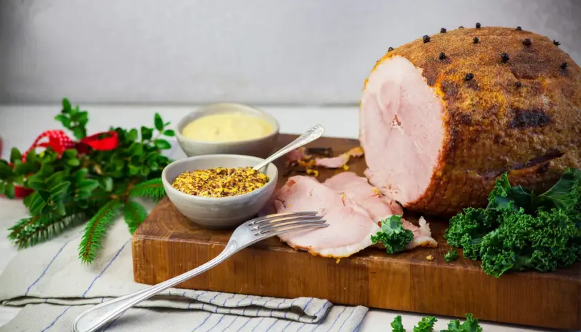 En saftig julskinka, redo att grilla, med senap och julpynt.