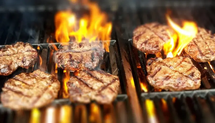 Flera saftiga hamburgare grillas på en gasolgrill med flammande eld.