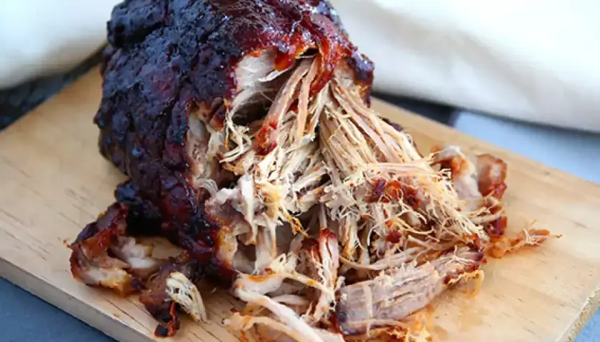 Saftigt, mörkt pulled pork på en skärbräda. Perfekt temperatur för att dra isär köttet.