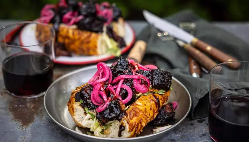 En saftig amerikansk barbeque-smörgås med möra köttbitar och picklad rödlök, serverad med rödvin.