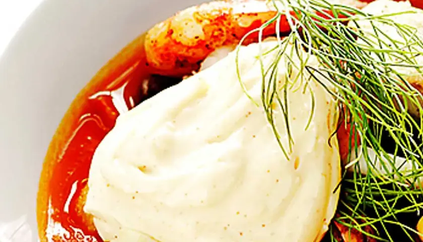 En närbild på en skål med räkor, dill och en generös klick egen aioli.