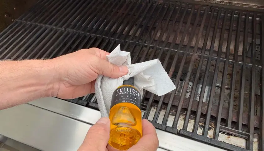 Händer oljar in grillgallret med en pappersduk och en flaska rapsolja för att maten inte ska fastna.