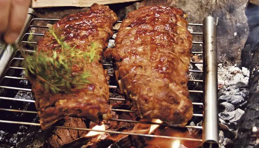 Två saftiga grillade spareribs på ett grillgaller över öppen eld. En kvist rosmarin läggs på för extra smak.