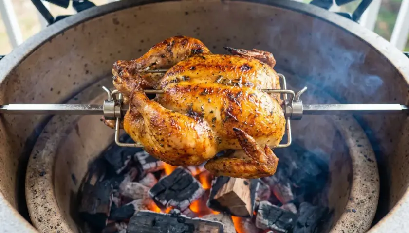 Hel kyckling grillas på rotisserie över glödande kol. En gyllene, saftig kyckling som doftar underbart.