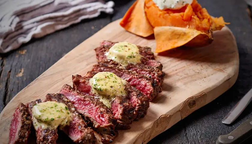 Skivad entrecote rare med smält örtsmör, serverad med sötpotatis och en klick gräddfil.
