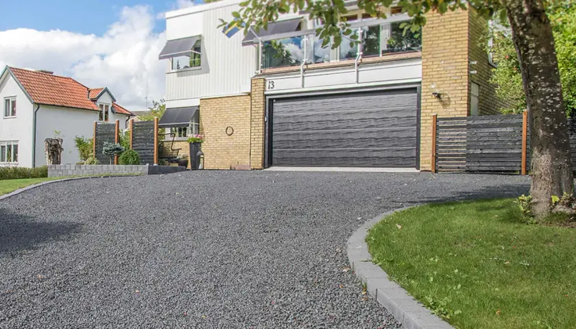 En grå stenlagd uppfart leder fram till ett modernt hus med garageport. Perfekt uppfart inspiration för en stilren entré.