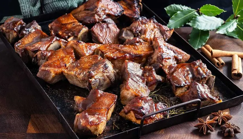 En bricka med saftiga revbensspjäll, täckta av en glansig revbens glaze. Kryddor som kanel och stjärnanis ligger bredvid.