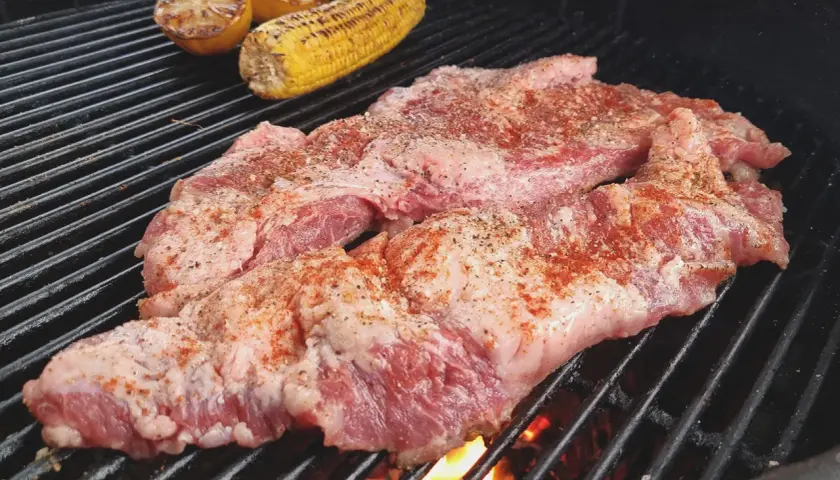 Två bitar grillad secreto med majskolv och citronklyftor på grillen.
