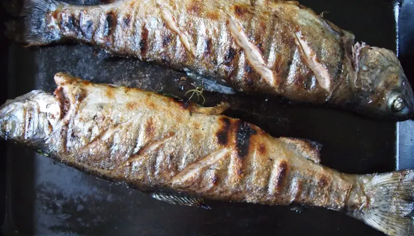 Två grillade saltlake fiskar ligger på en svart plåt. De har fått fina grillränder och ser saftiga ut.